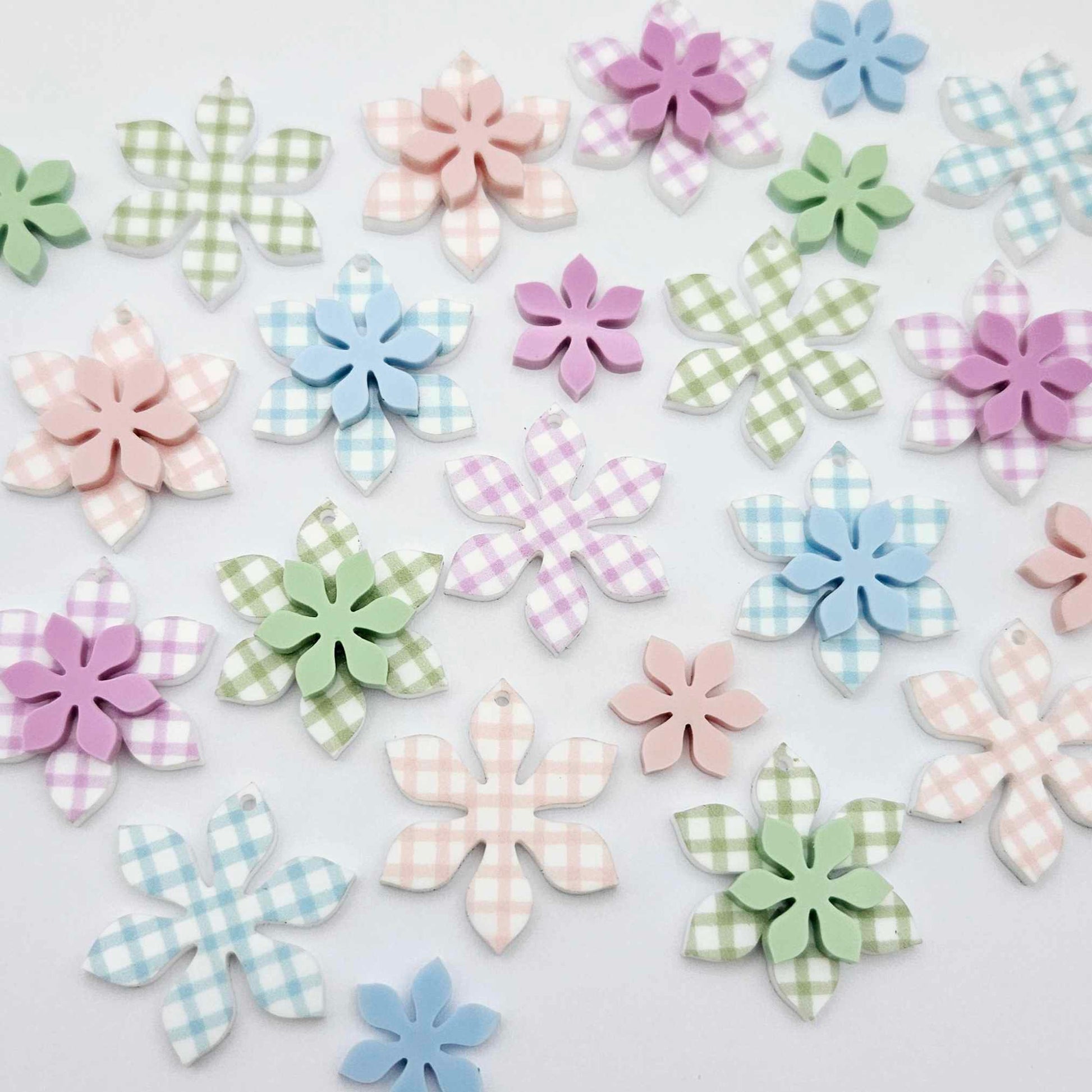 Gingham UV print and pastel acrylic two layer flower dangle blanks shown laying flat, with some flowers stacked to show layered effect and others positioned side by side