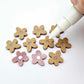 16mm dusty rose organic flower stud blanks showing paint filled white example and unfilled pieces with protective film, pictured with a white Posca paint pen