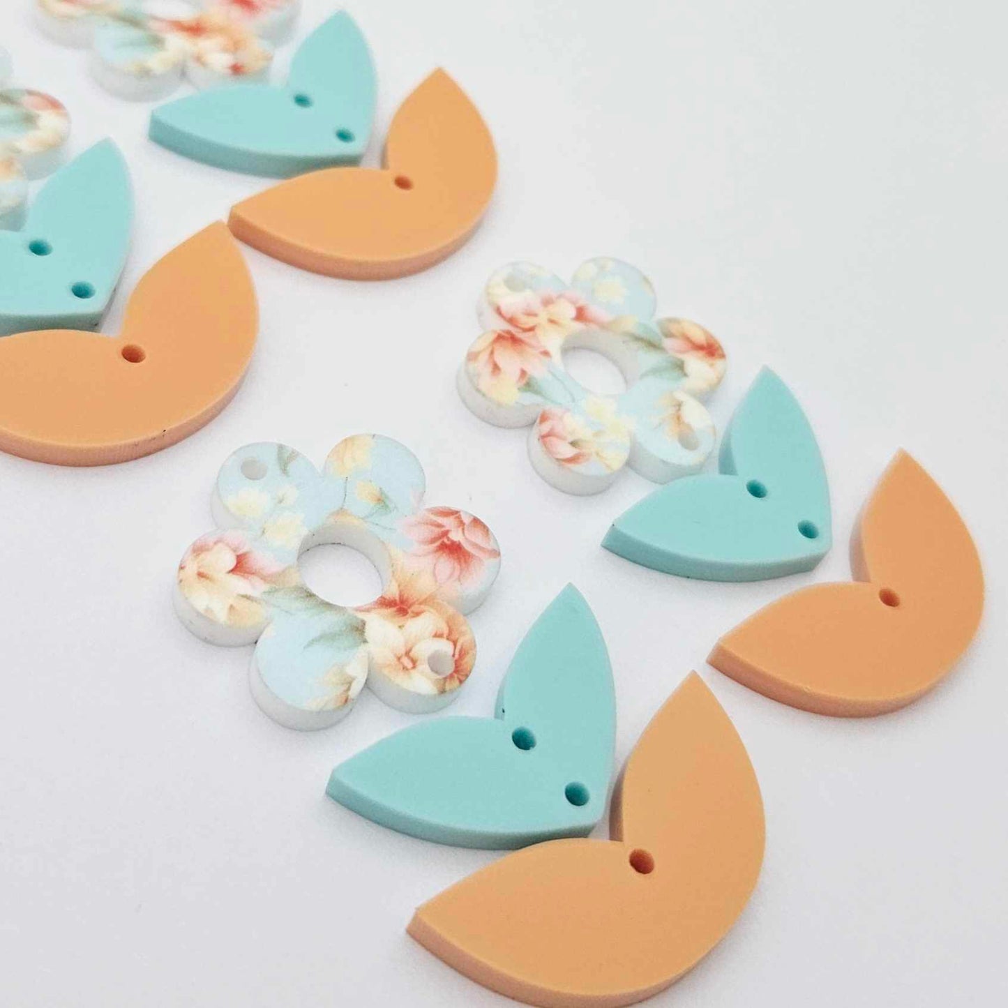 Three-piece acrylic flower dangle blanks shown unassembled laying flat, featuring Floral Bloom UV printed flower, aqua leafy middle and orange leafy bottom