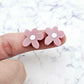 Two 16mm dusty rose organic flower stud blanks with engraved centre paint filled white, shown on a finger for size reference
