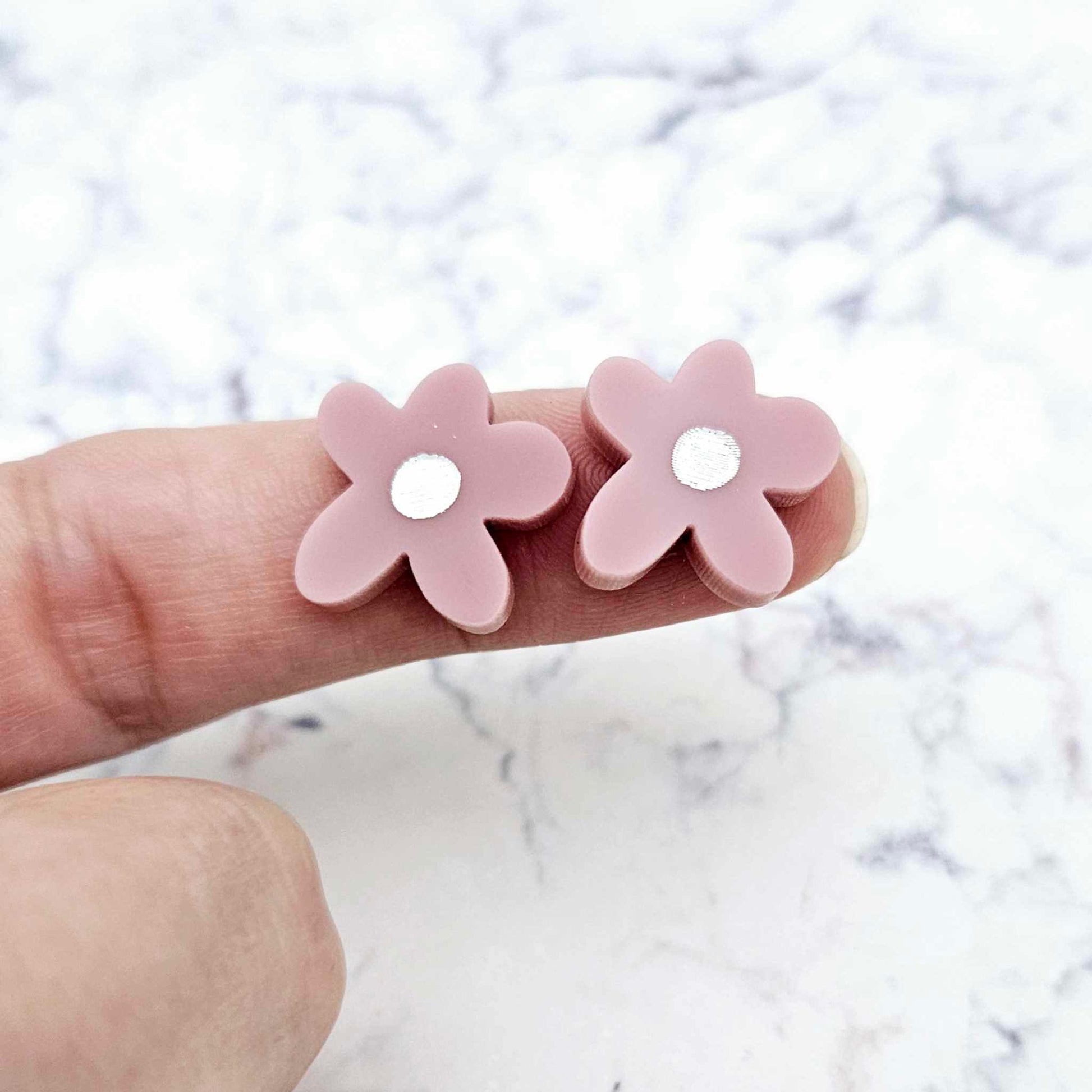 Two 16mm dusty rose organic flower stud blanks with engraved centre paint filled white, shown on a finger for size reference