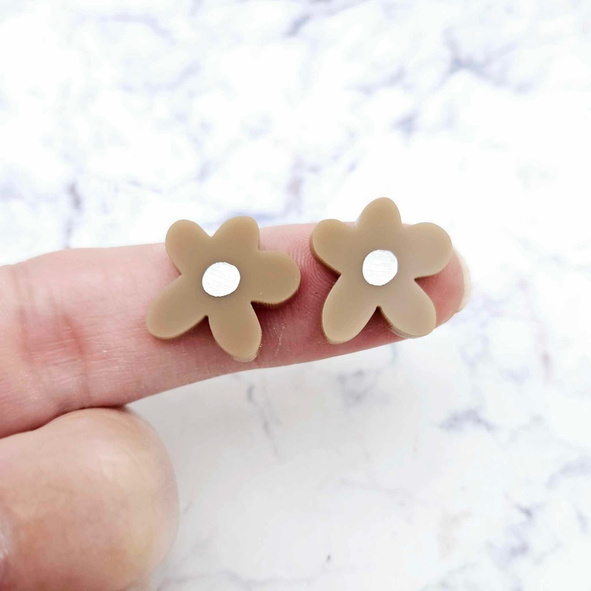 Two 16mm iced coffee brown organic flower stud blanks with engraved centre paint filled white, shown on a finger for size reference