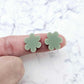 Two 14mm olive green flower stud blanks, shown on a finger for size reference