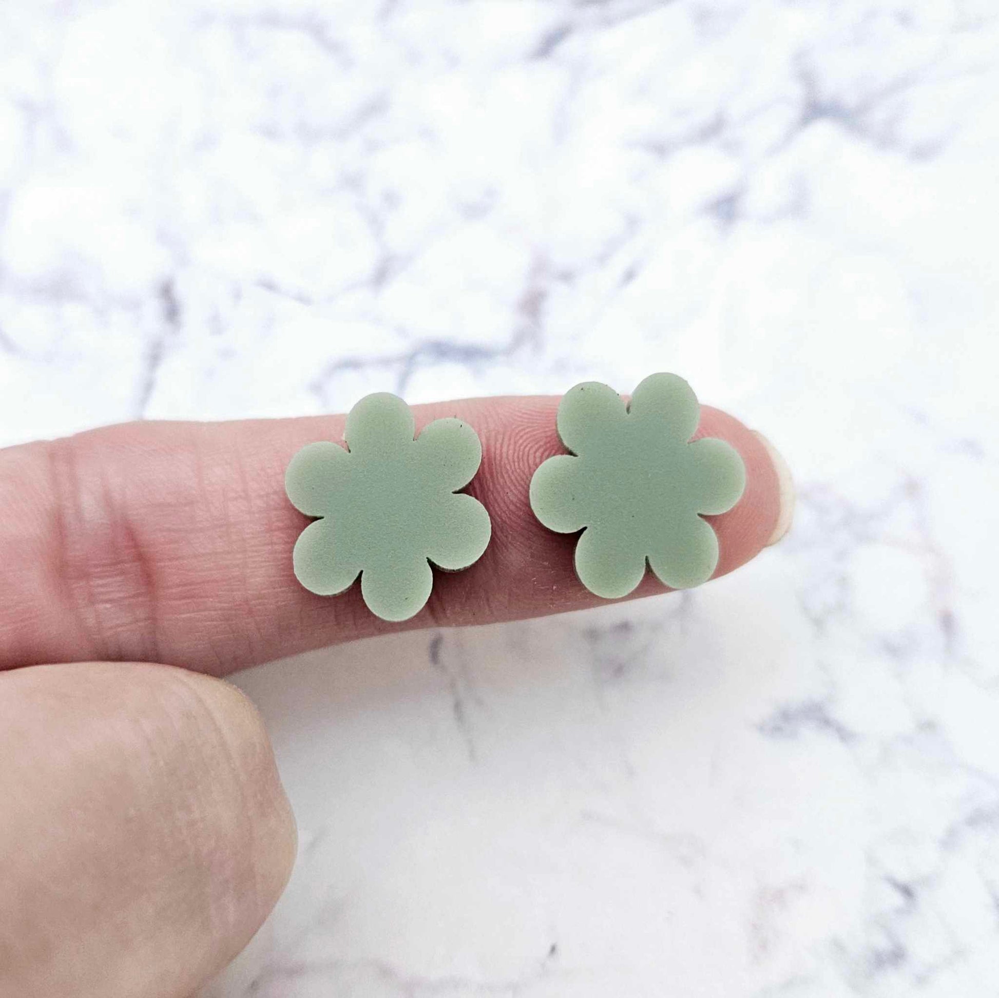 Two 14mm olive green flower stud blanks, shown on a finger for size reference