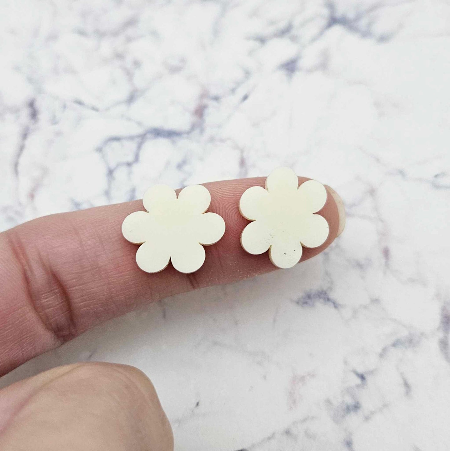 Two 14mm cream acrylic flower stud blanks, shown on a finger for size reference