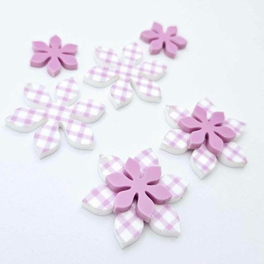 Purple gingham UV print and sour grape acrylic two layer flower dangle blanks shown laying flat, with some flowers stacked to show layered effect and others positioned side by side