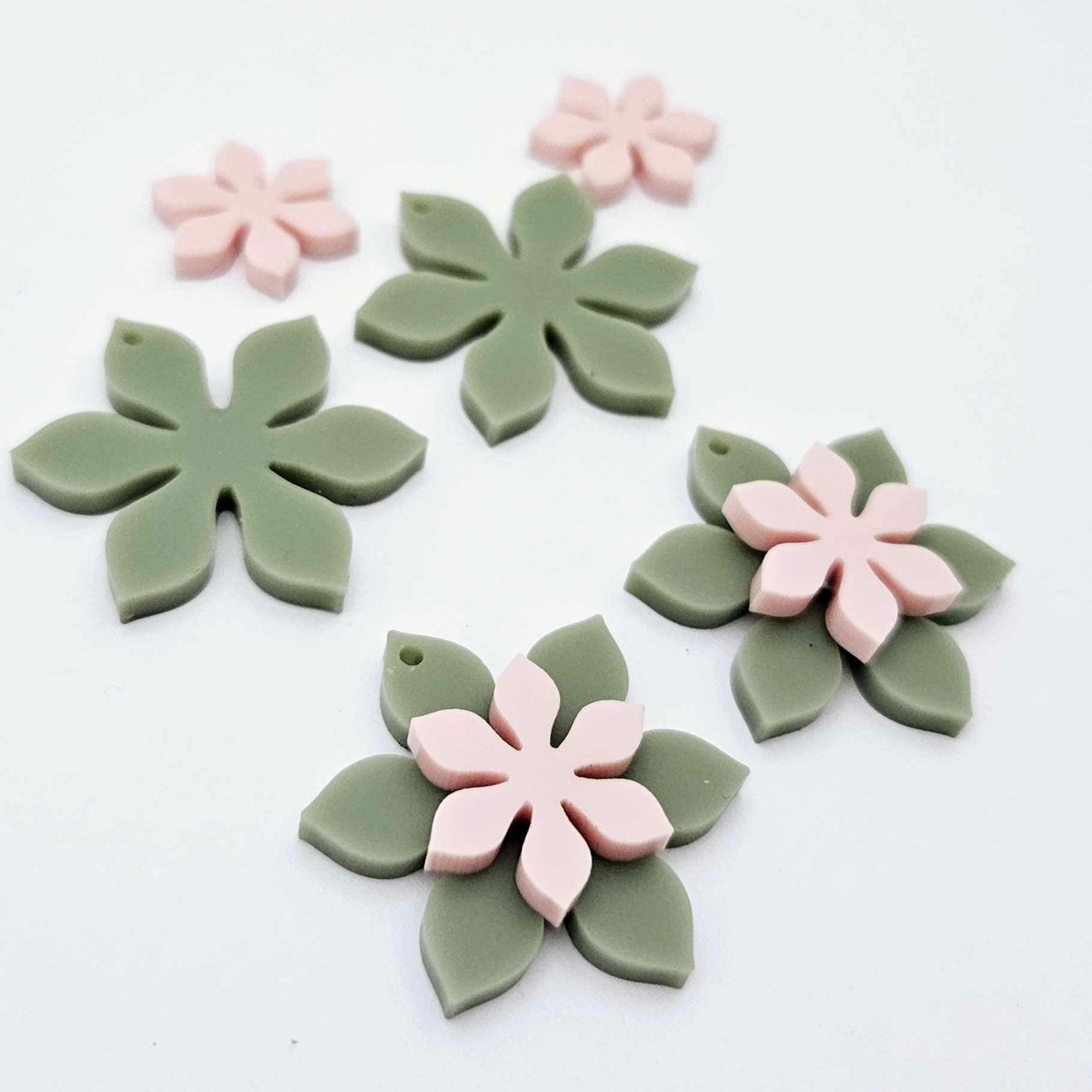 Olive Green and strawberry milkshake pink acrylic two layer flower dangle blanks shown laying flat, with some flowers stacked to show layered effect and others positioned side by side