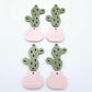Two-piece cactus dangle blanks in olive green and strawberry milkshake pink, shown unassembled with cactus top and pot bottom pieces laid flat