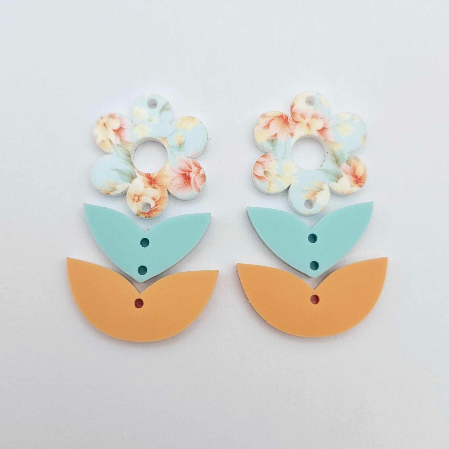 Three-piece acrylic flower dangle blanks shown unassembled laying flat, featuring Floral Bloom UV printed flower, aqua leafy middle and orange leafy bottom