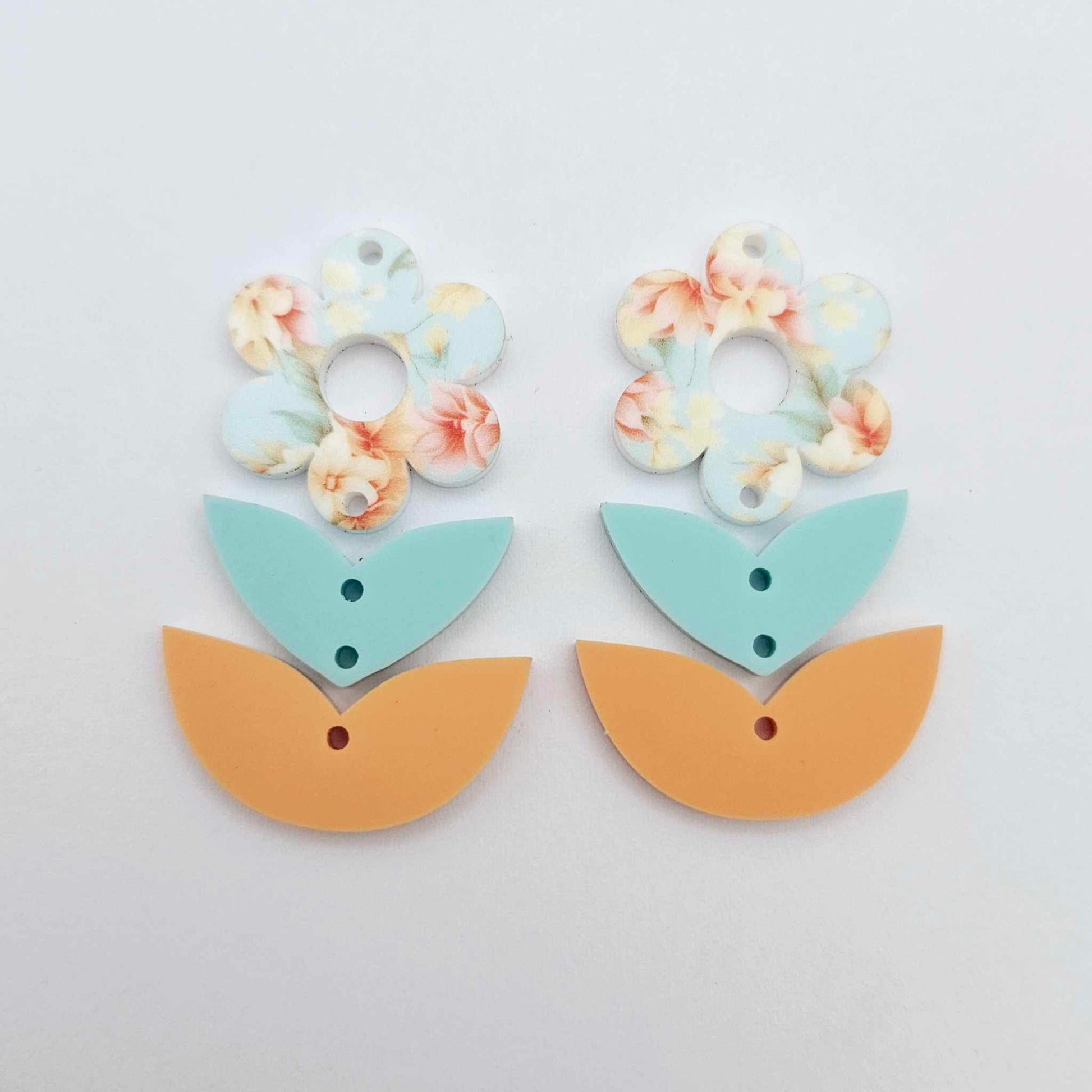 Three-piece acrylic flower dangle blanks shown unassembled laying flat, featuring Floral Bloom UV printed flower, aqua leafy middle and orange leafy bottom