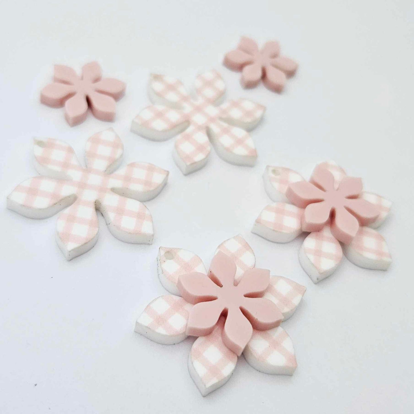 Pink gingham UV print and strawberry milkshake pink acrylic two layer flower dangle blanks shown laying flat, with some flowers stacked to show layered effect and others positioned side by side