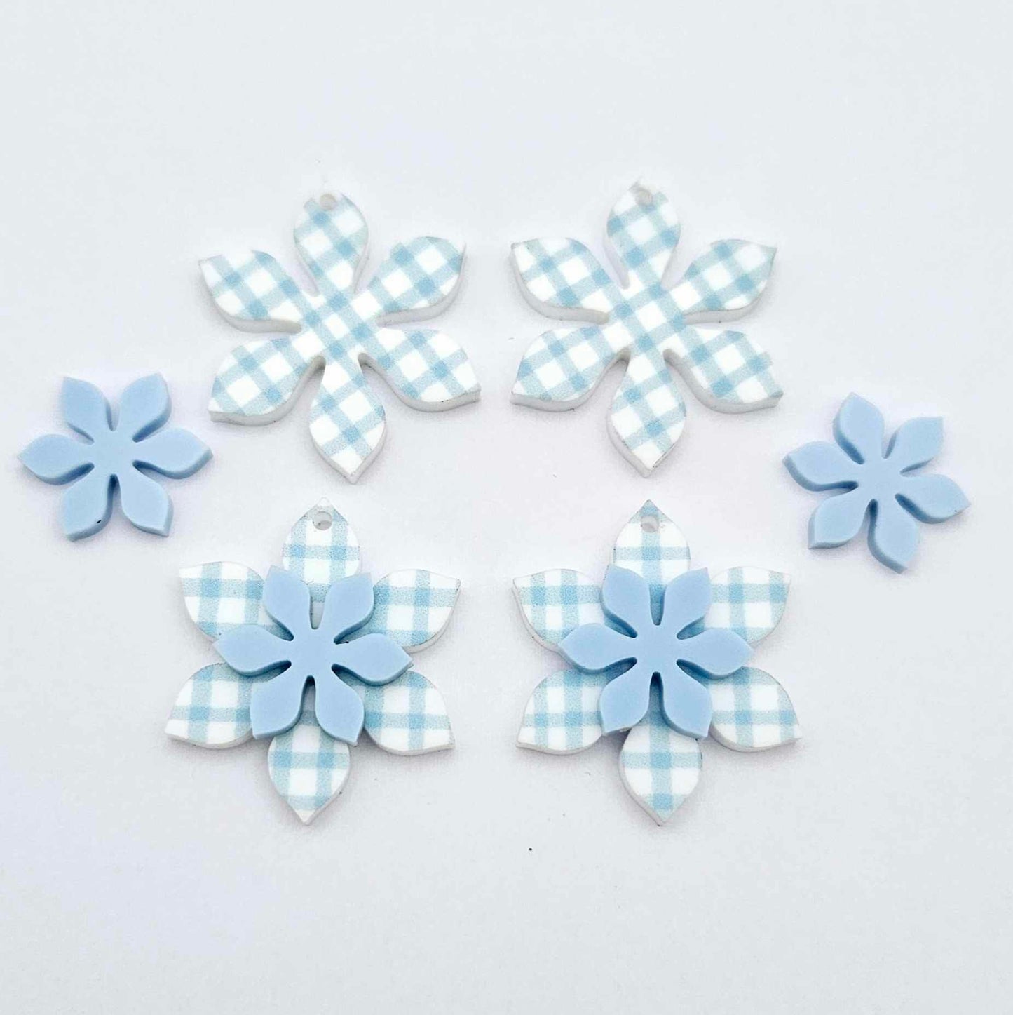 Blue gingham UV print and pastel blue acrylic two layer flower dangle blanks shown laying flat, with some flowers stacked to show layered effect and others positioned side by side