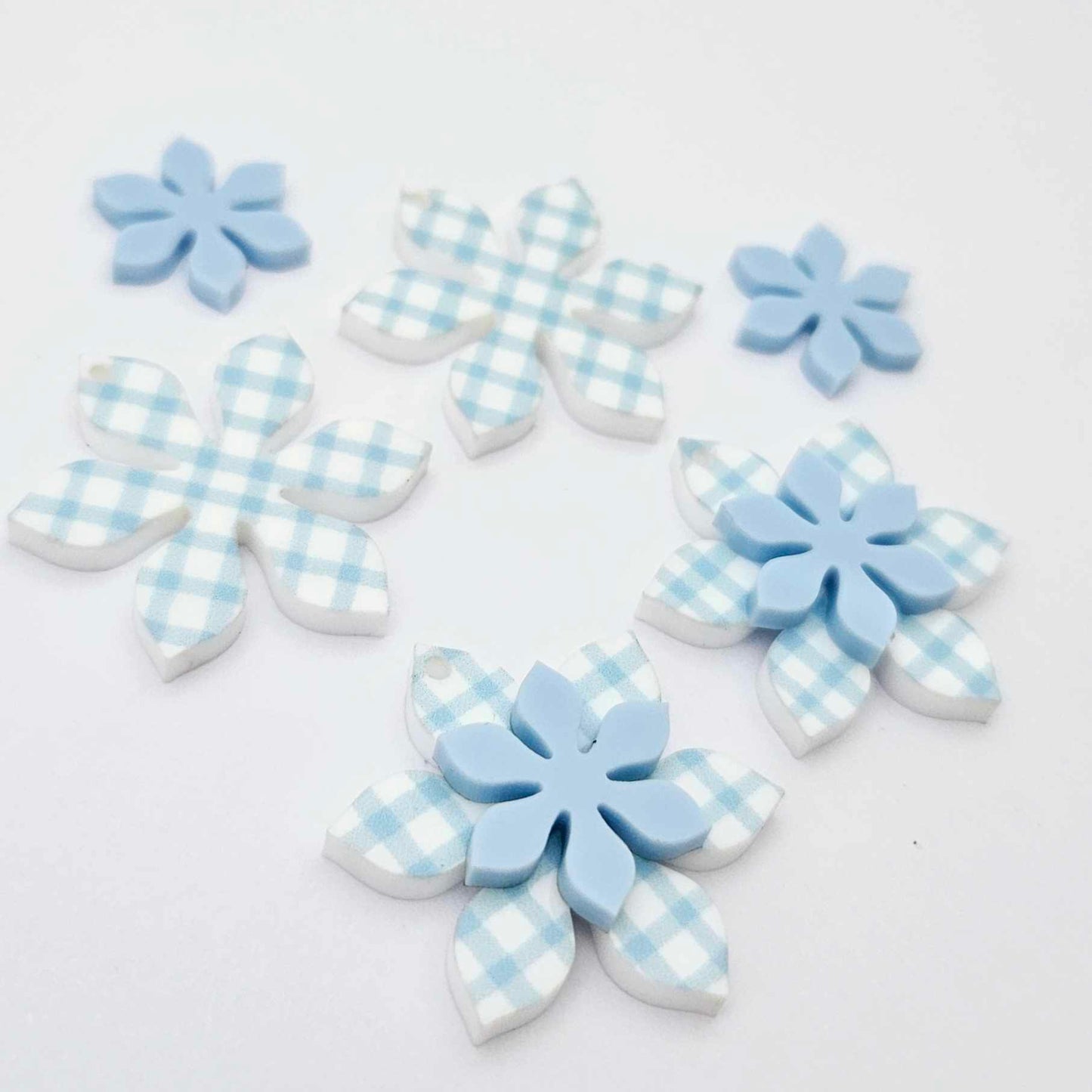 Blue gingham UV print and pastel blue acrylic two layer flower dangle blanks shown laying flat, with some flowers stacked to show layered effect and others positioned side by side
