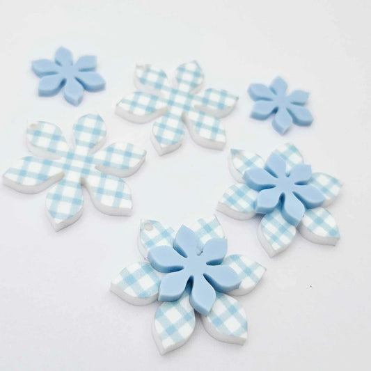Blue gingham UV print and pastel blue acrylic two layer flower dangle blanks shown laying flat, with some flowers stacked to show layered effect and others positioned side by side