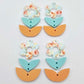 Three-piece acrylic flower dangle blanks shown unassembled laying flat, featuring Floral Bloom UV printed flower, aqua leafy middle and orange leafy bottom