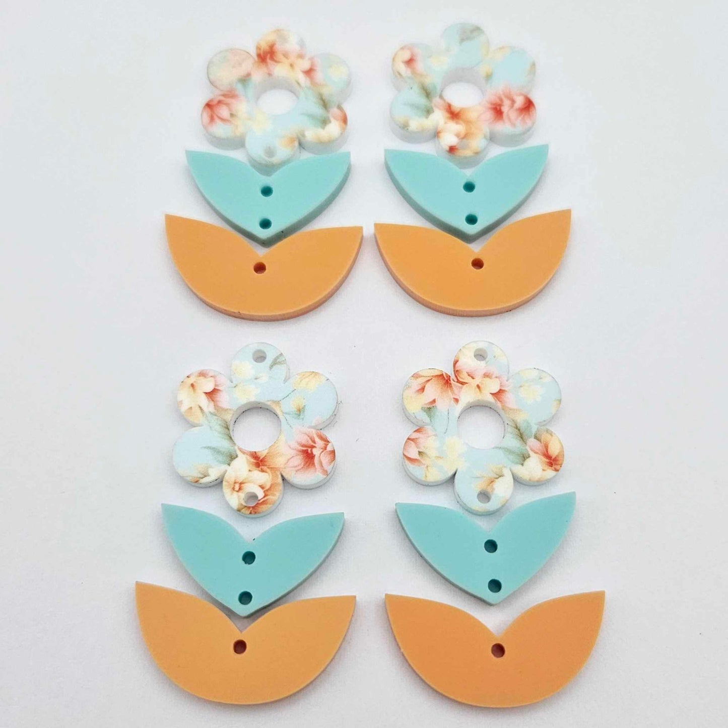 Three-piece acrylic flower dangle blanks shown unassembled laying flat, featuring Floral Bloom UV printed flower, aqua leafy middle and orange leafy bottom