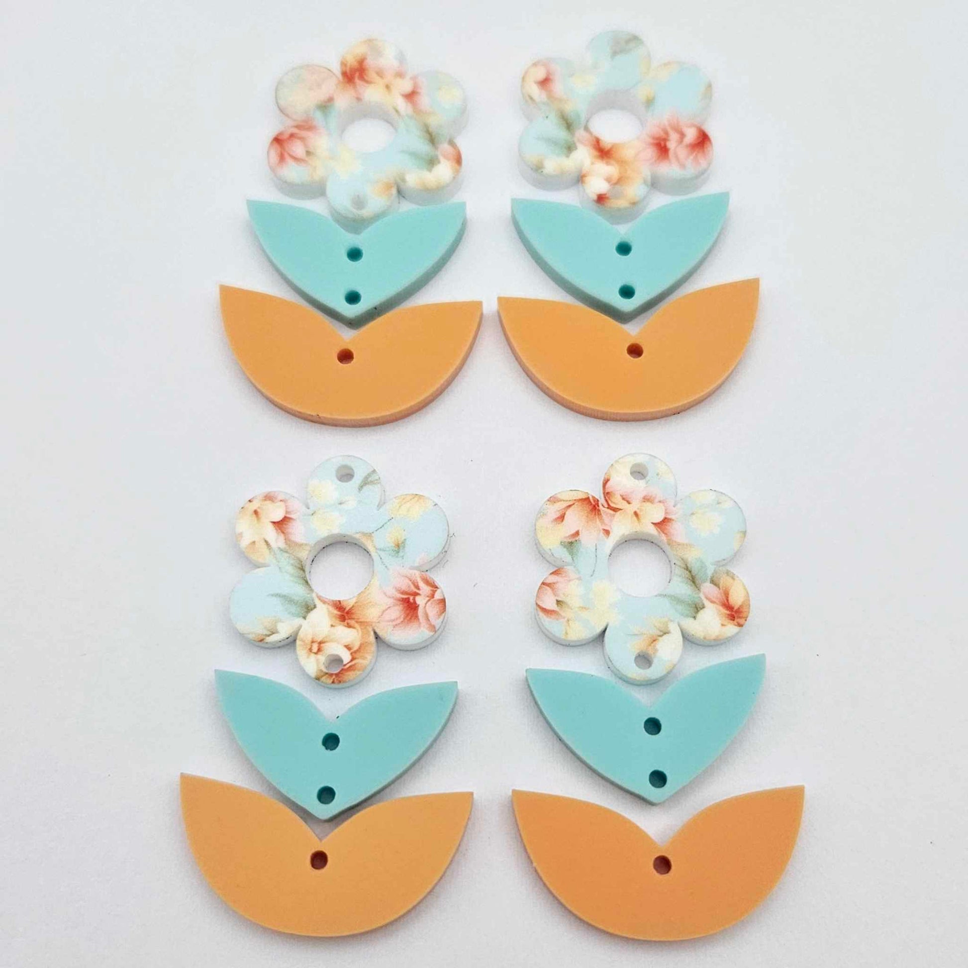 Three-piece acrylic flower dangle blanks shown unassembled laying flat, featuring Floral Bloom UV printed flower, aqua leafy middle and orange leafy bottom
