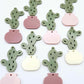 Two-piece acrylic cactus dangle blanks in olive green with mixed coloured pots, shown unassembled with cactus top and pot bottom pieces laid flat