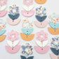 Three-piece acrylic flower dangle blanks shown unassembled laying flat, featuring  UV printed flower, solid colour leafy middle and bottom pieces