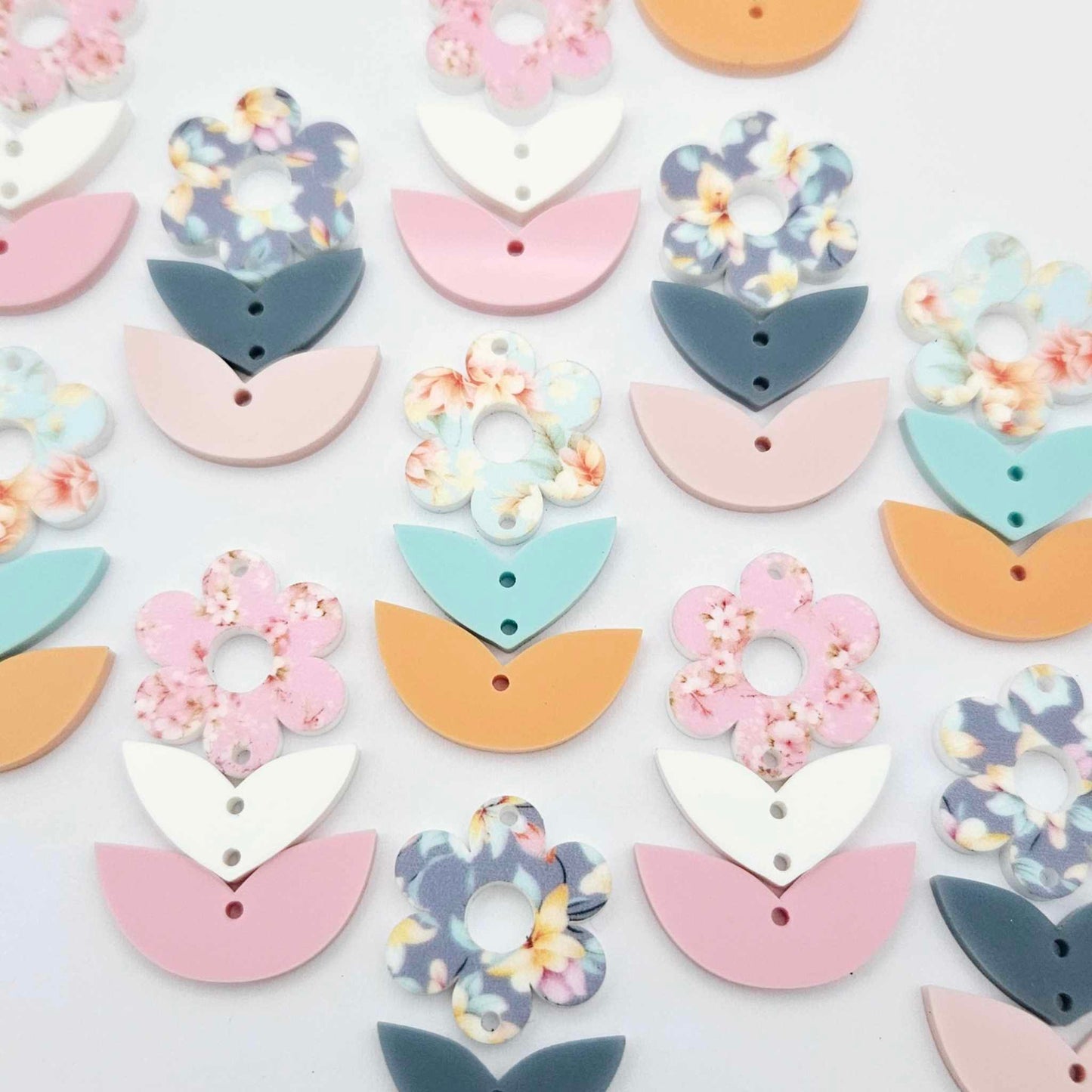 Three-piece acrylic flower dangle blanks shown unassembled laying flat, featuring  UV printed flower, solid colour leafy middle and bottom pieces