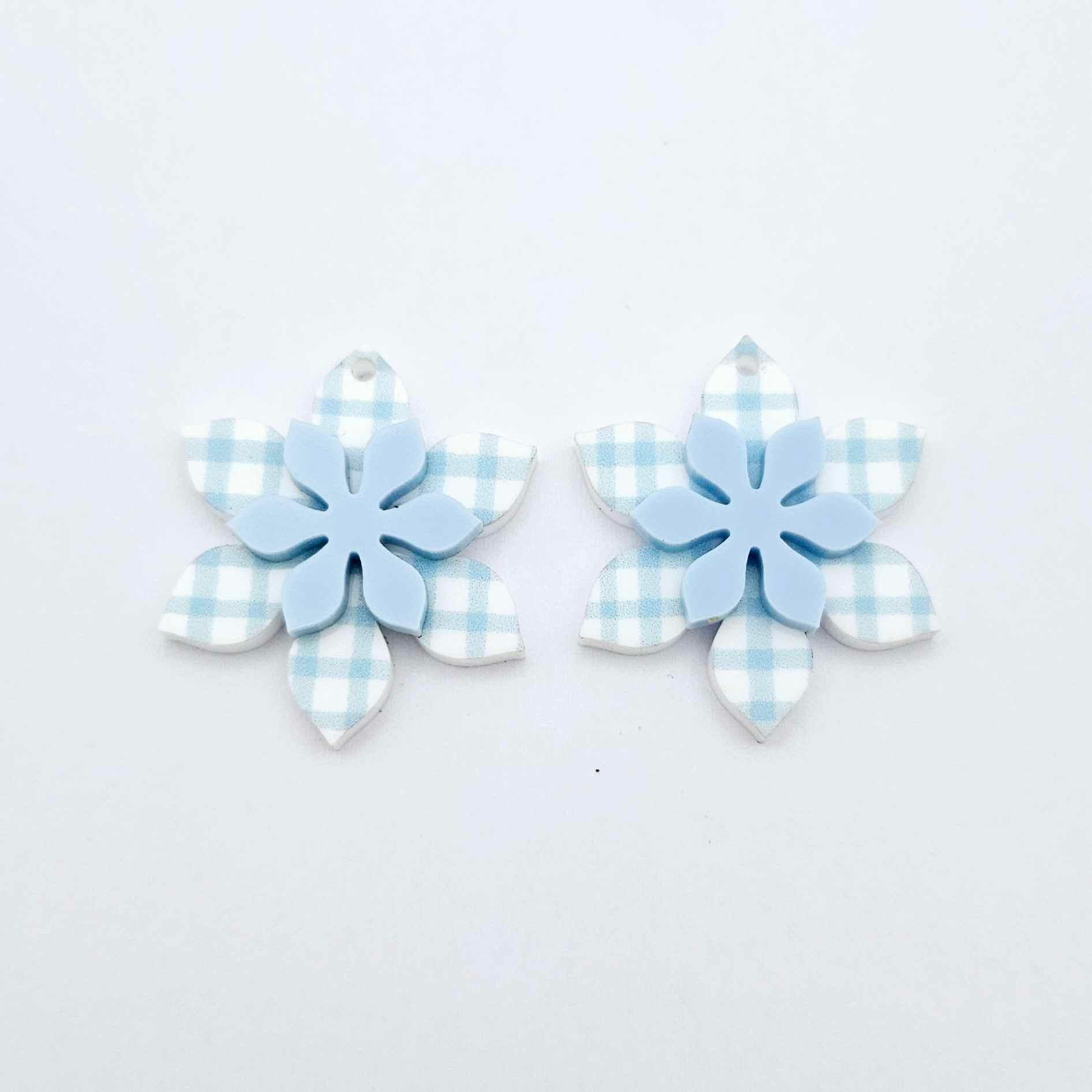 Blue gingham UV print and pastel blue acrylic two layer flower dangle blanks shown laying flat, with some flowers stacked to show layered effect and others positioned side by side