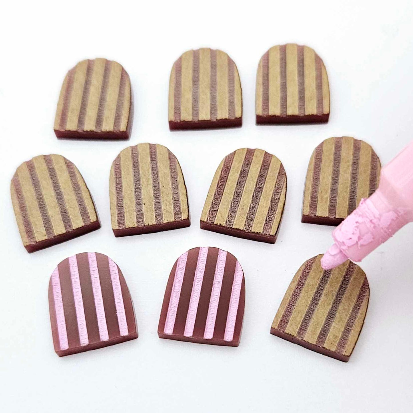 16mm port wine striped acrylic arch stud blanks showing paint filled example and unpainted pieces with protective film, pictured with a light pink Posca paint pen
