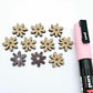 Chocolate brown acrylic flower stud blanks showing paint filled light pink example and unpainted pieces with protective film, pictured with a light pink Posca paint pen