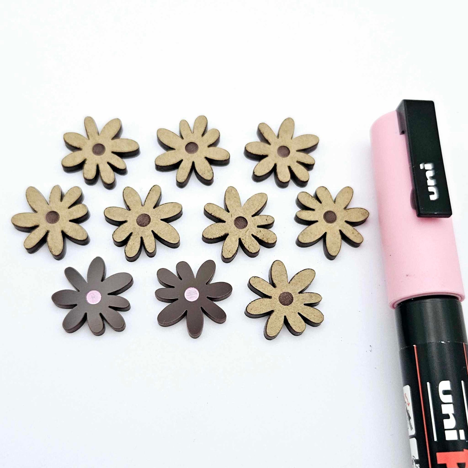 Chocolate brown acrylic flower stud blanks showing paint filled light pink example and unpainted pieces with protective film, pictured with a light pink Posca paint pen