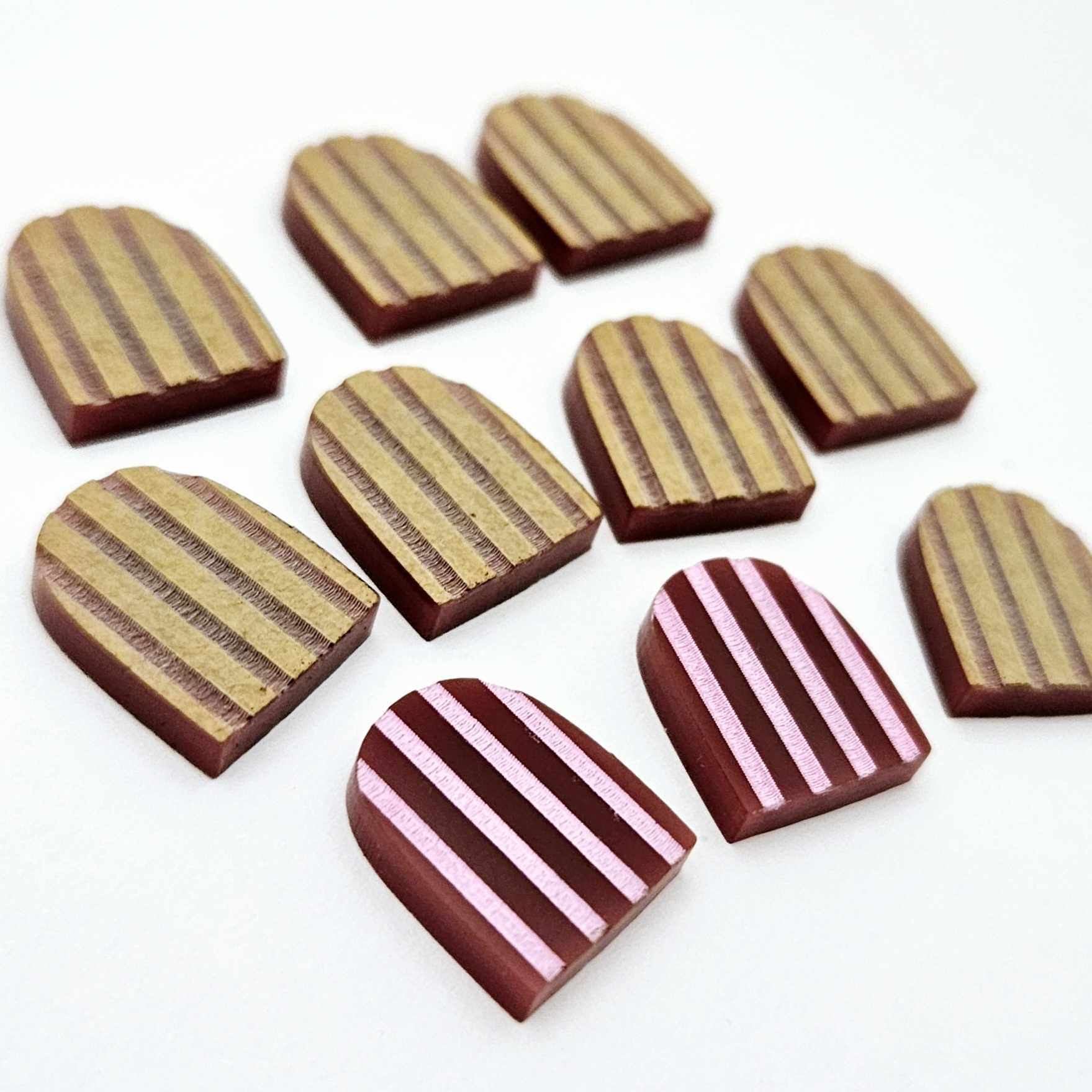 Port wine striped arch stud blanks with engraved stripes, one pair paint filled light pink and peeled, with additional unpainted pieces shown with protective film on
