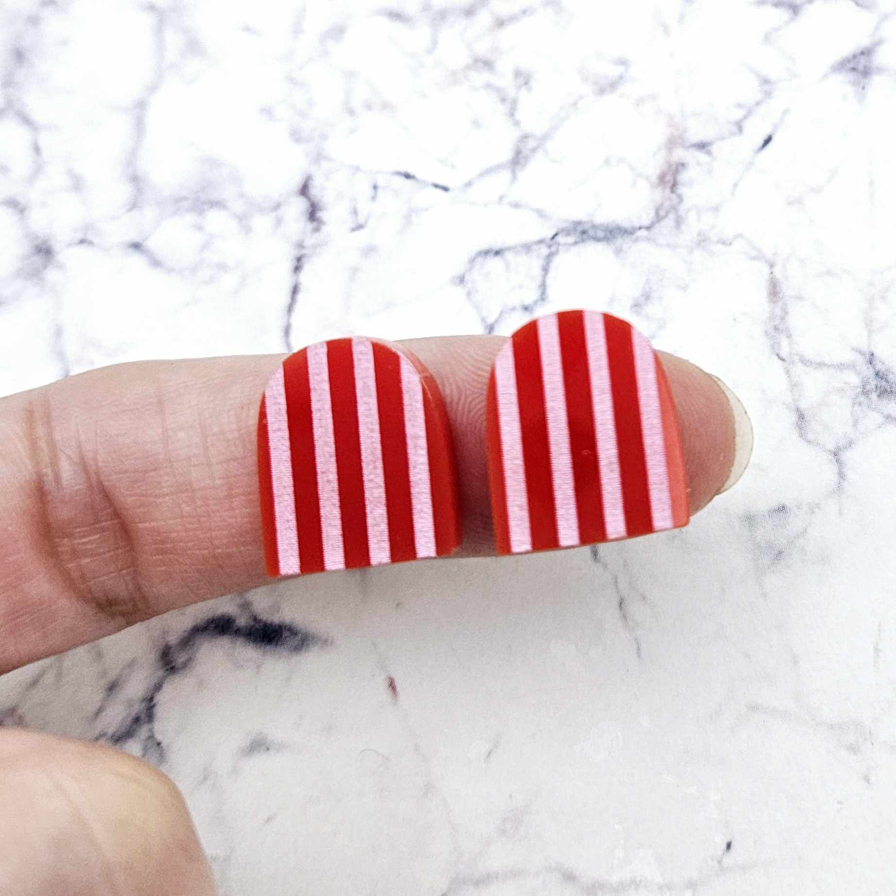 16mm red striped arch acrylic stud blanks paint filled with light pink, shown on a finger for size reference and finished look