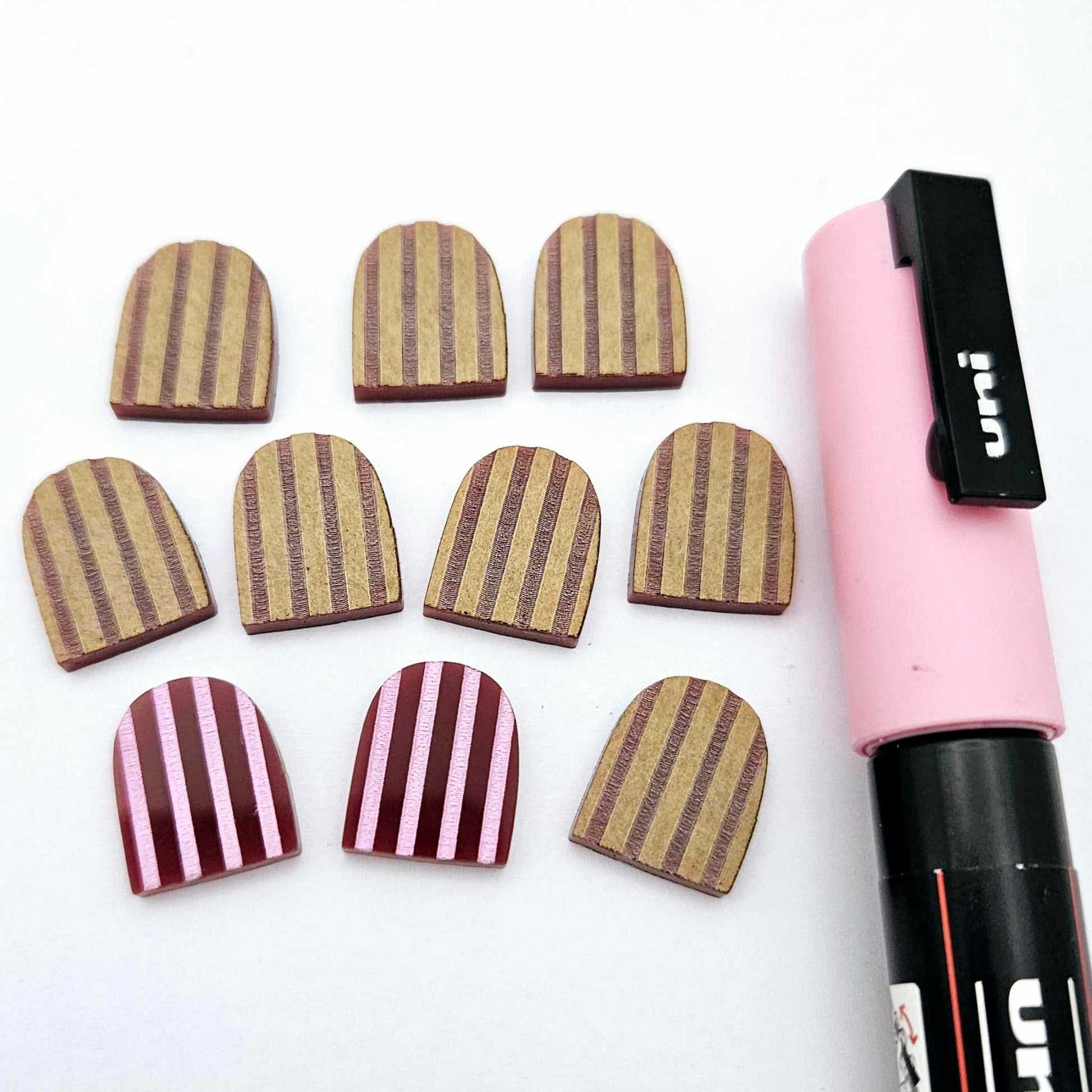 16mm port wine striped acrylic arch stud blanks showing paint filled example and unpainted pieces with protective film, pictured with a light pink Posca paint pen