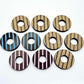 22mm chocolate brown acrylic striped hoop stud blanks with engraved stripes, one pair paint filled light pink and one light blue and peeled, with additional unpainted pieces shown with protective film on