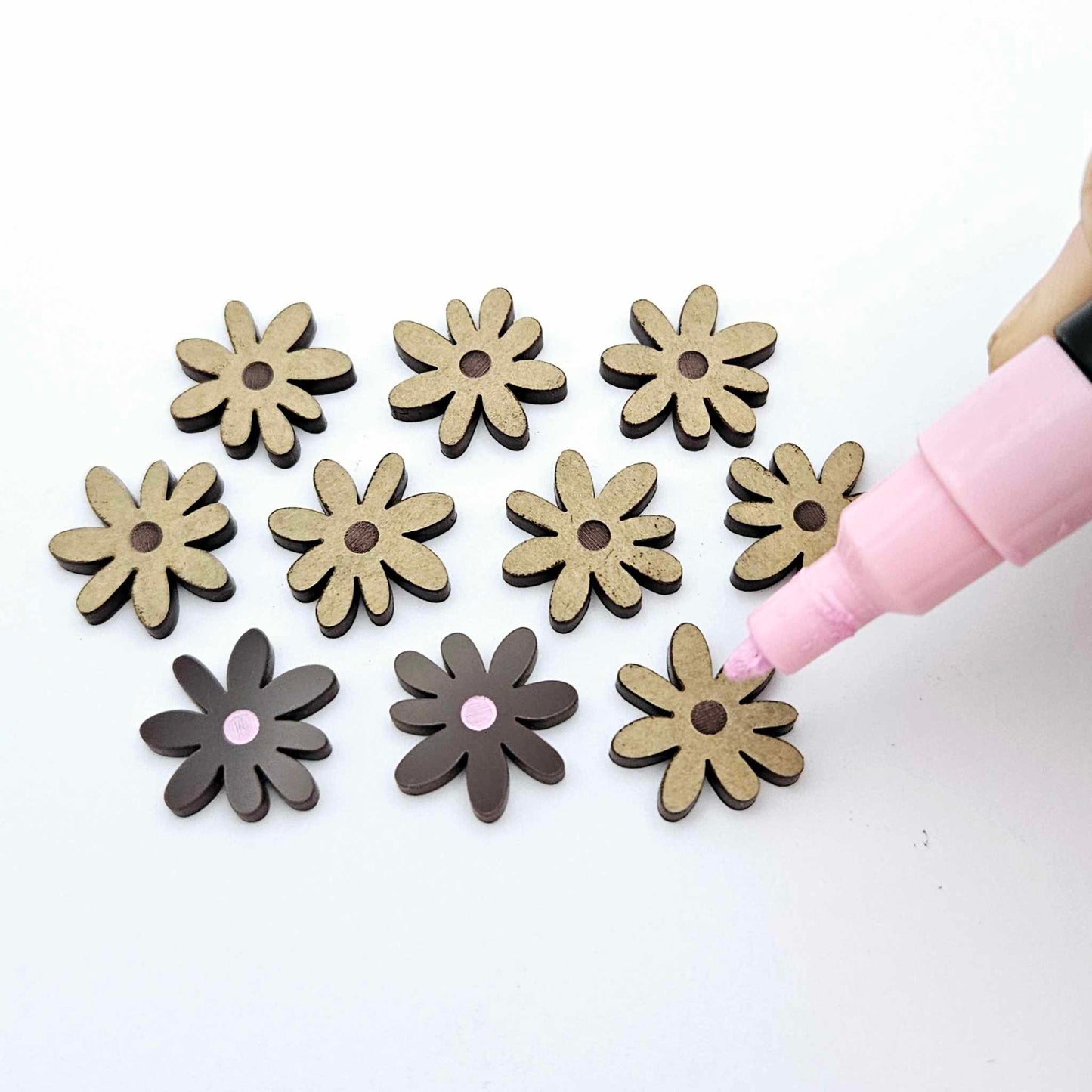Chocolate brown acrylic flower stud blanks showing paint filled light pink example and unpainted pieces with protective film, pictured with a light pink Posca paint pen