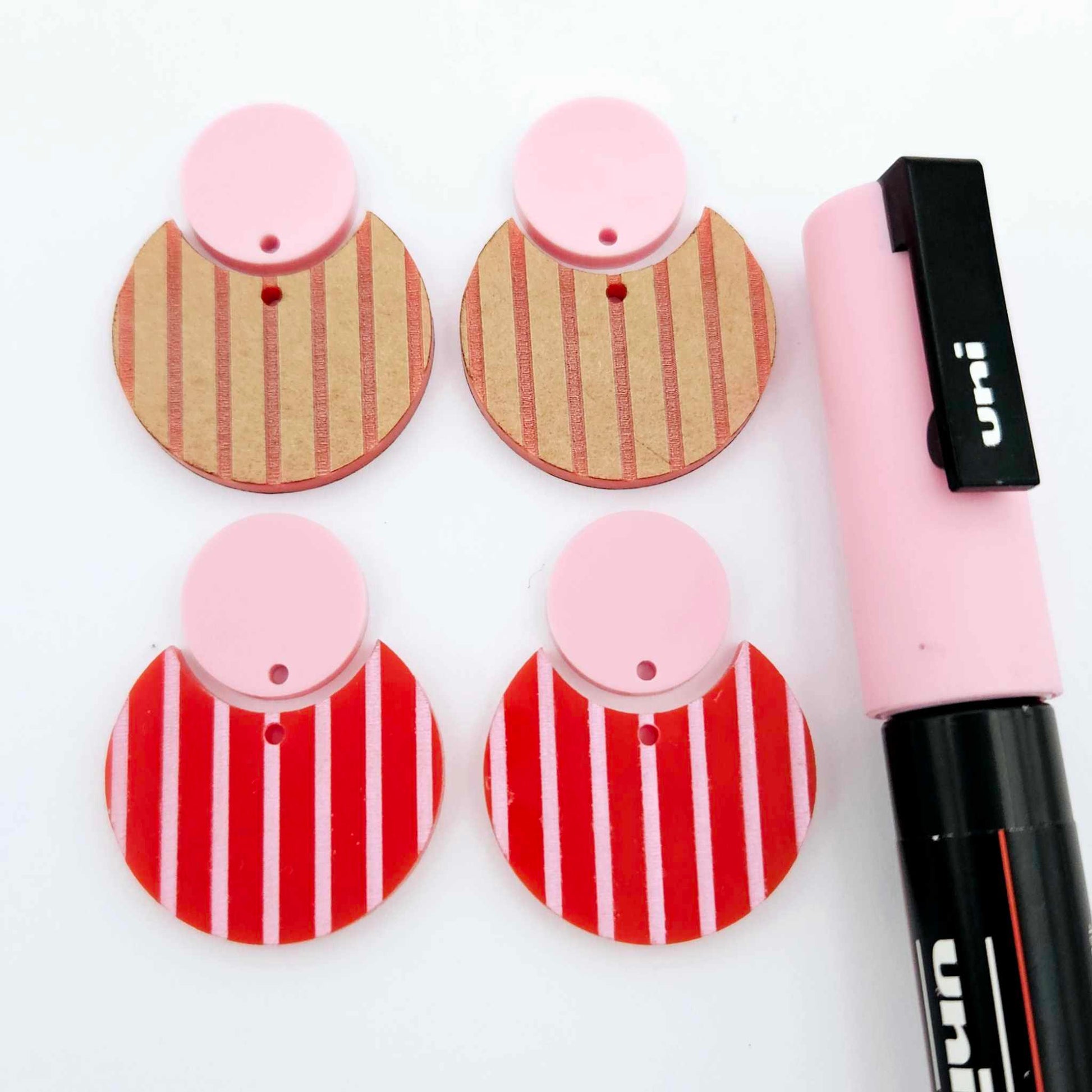 Nested circle dangle blanks showing one pair paint filled light pink and peeled, with another pair unpainted and with protective film on, pictured with a pink Posca paint pen
