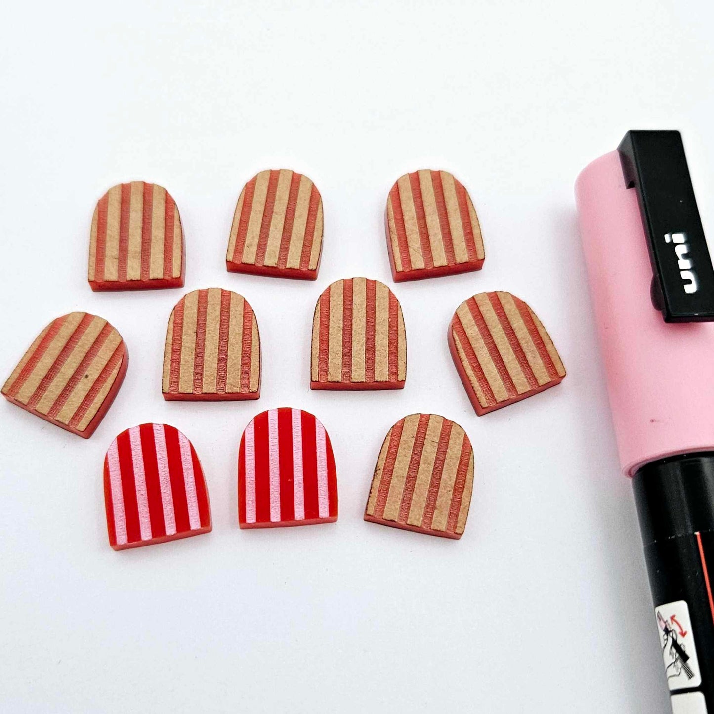 16mm red striped acrylic arch stud blanks showing paint filled example and unpainted pieces with protective film, pictured with a light pink Posca paint pen