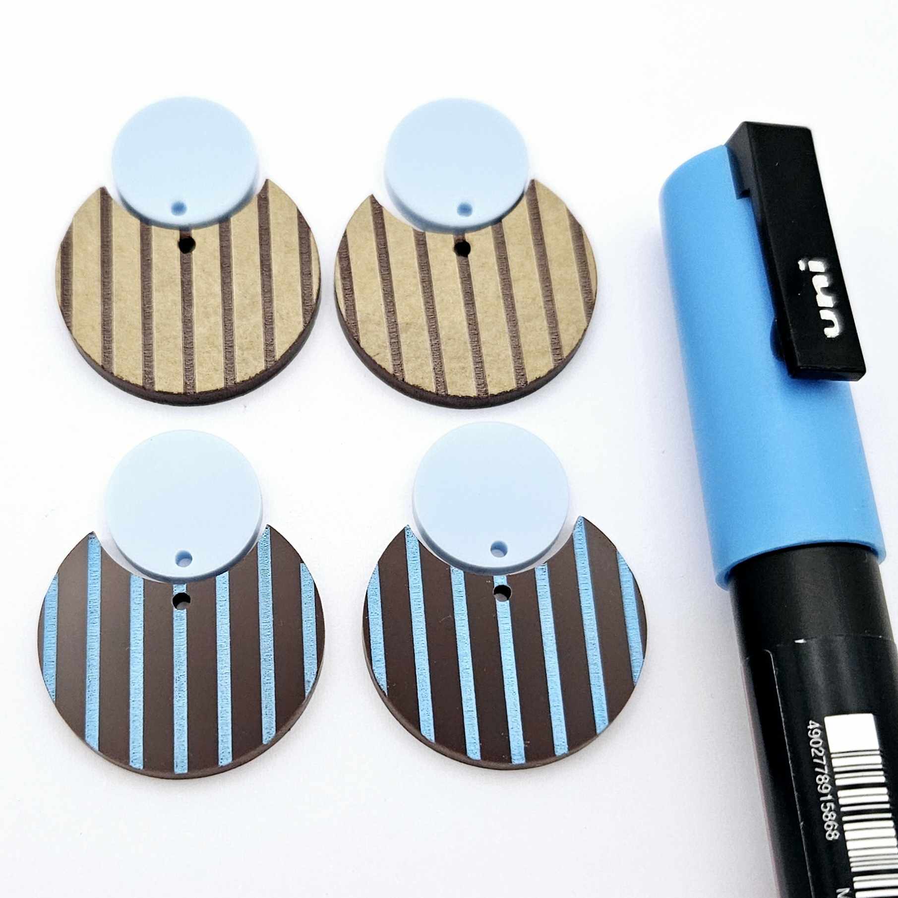 Nested circle dangle blanks showing one piece paint filled light blue and peeled, with another pair unpainted and with protective film on, pictured with a light blue Posca paint pen