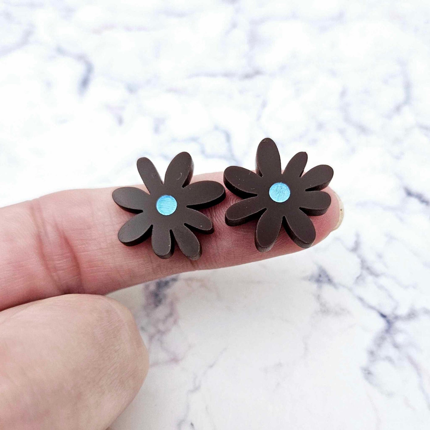17mm chocolate brown acrylic flower stud blanks with engraved centre detail, one pair paint filled light blue shown on finger for size reference