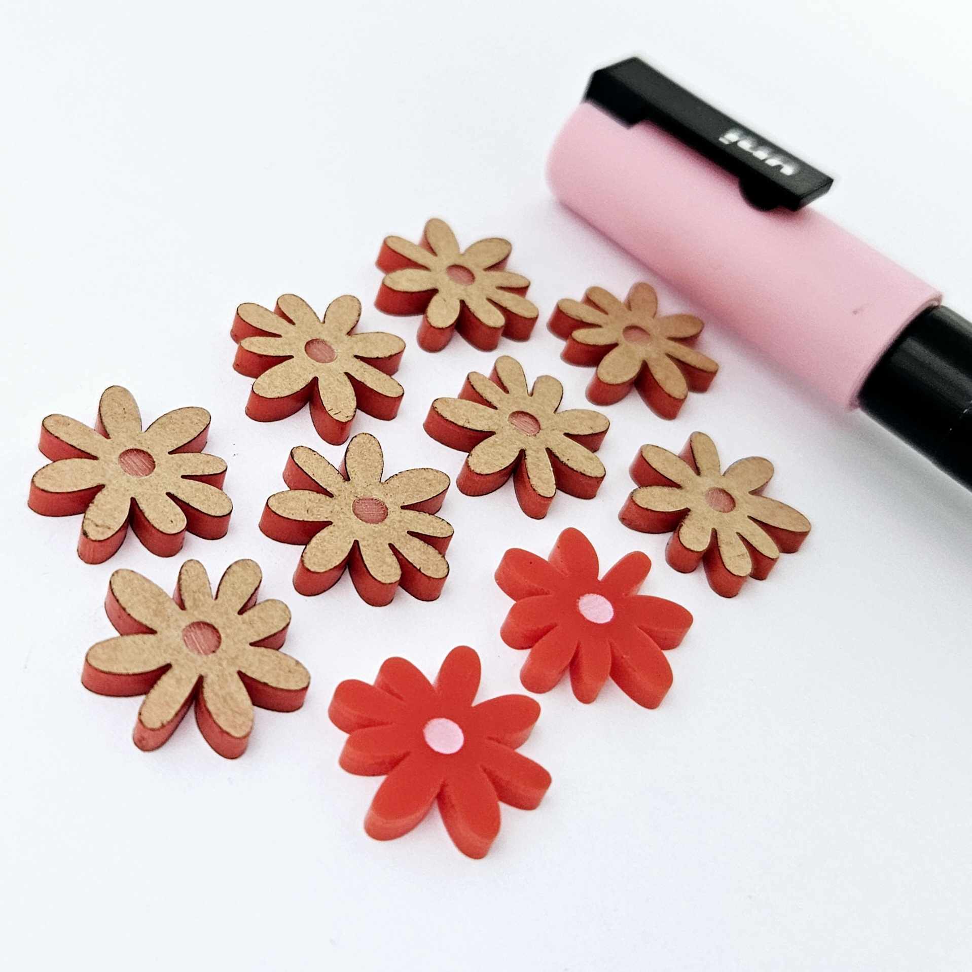 Red acrylic flower stud blanks showing paint filled light pink example and unpainted pieces with protective film, pictured with a light pink Posca paint pen