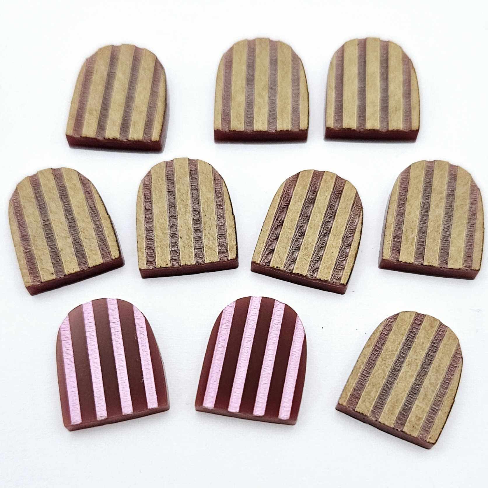 Port wine striped arch stud blanks with engraved stripes, one pair paint filled light pink and peeled, with additional unpainted pieces shown with protective film on