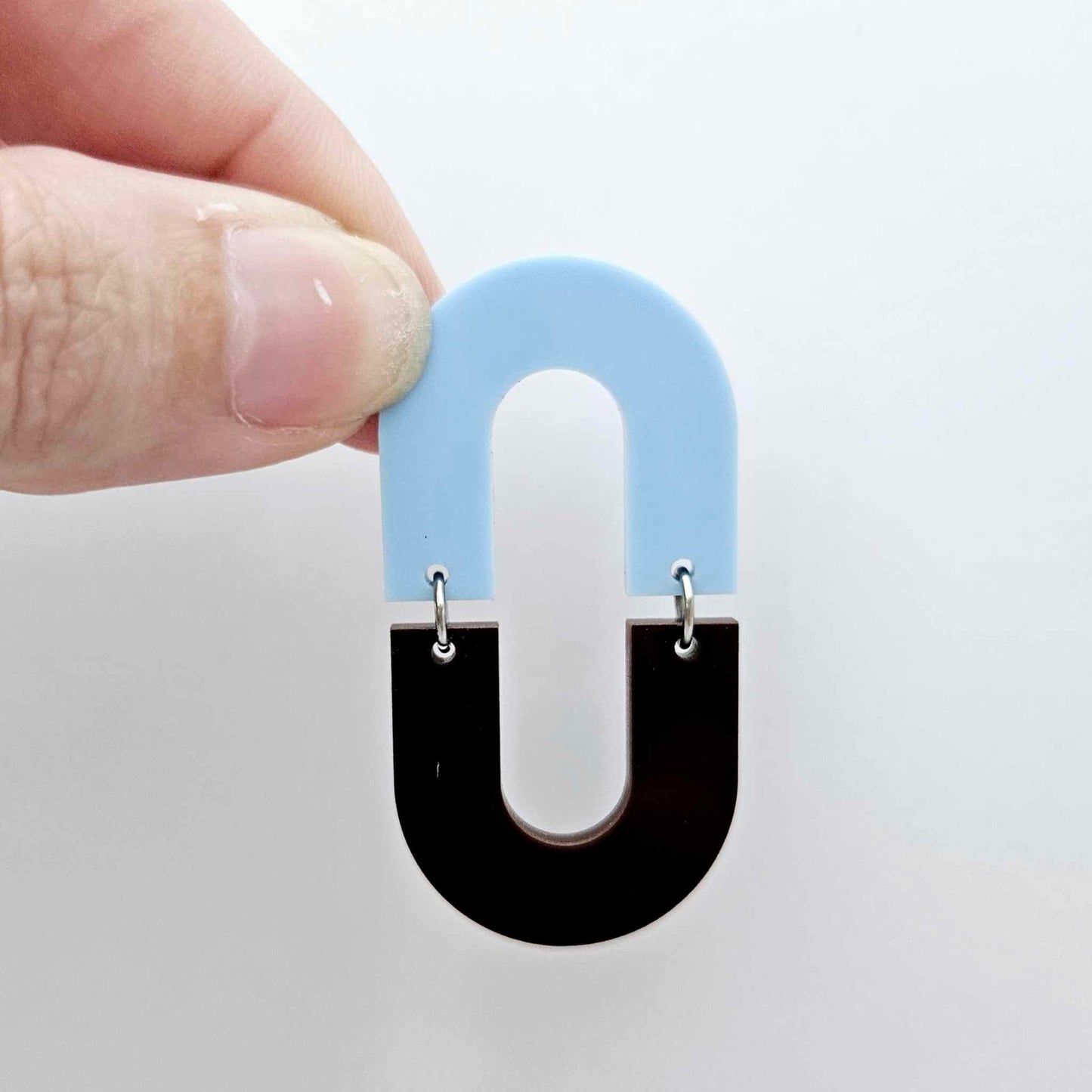 Layered U shape dangle earring in pastel blue and chocolate brown acrylic, assembled into an open oval design hanging as a statement stud dangle