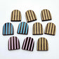 Chocolate brown striped arch stud blanks with engraved stripes, one pair paint filled light pink, one pair painted filled light blue, with additional unpainted pieces shown with protective film on