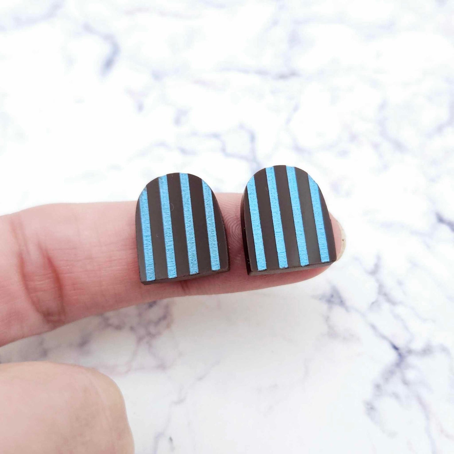 16mm chocolate brown striped arch acrylic stud blanks paint filled with light blue, shown on a finger for size reference and finished look
