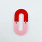 Layered U shape dangle earring in pastel pink and red acrylic, assembled into an open oval design hanging as a statement stud dangle