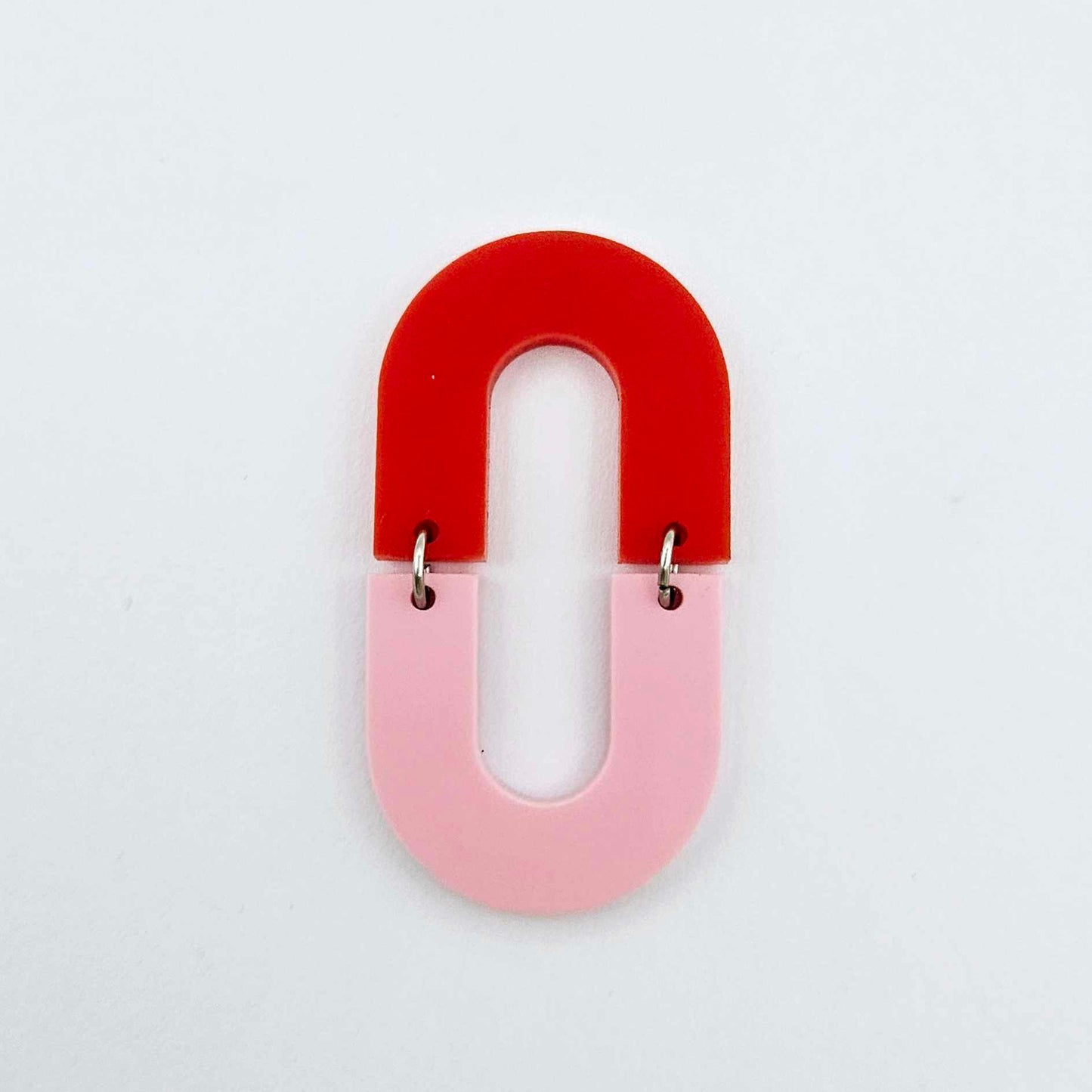 Layered U shape dangle earring in pastel pink and red acrylic, assembled into an open oval design hanging as a statement stud dangle