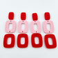 Two pairs of layered rectangle dangle blanks in red and pastel pink acrylic, unassembled pieces laid flat showing three-piece design