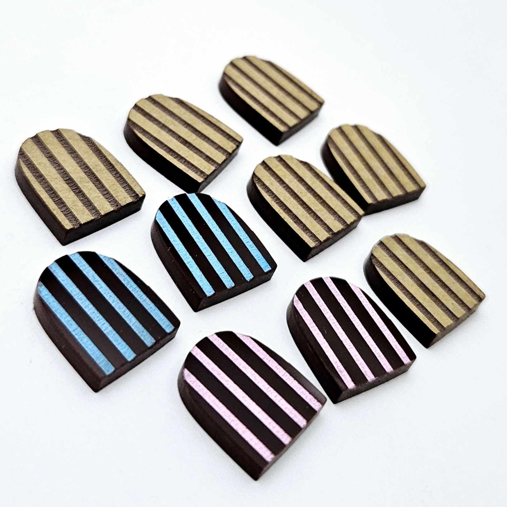 Chocolate brown striped arch stud blanks with engraved stripes, one pair paint filled light pink, one pair painted filled light blue, with additional unpainted pieces shown with protective film on