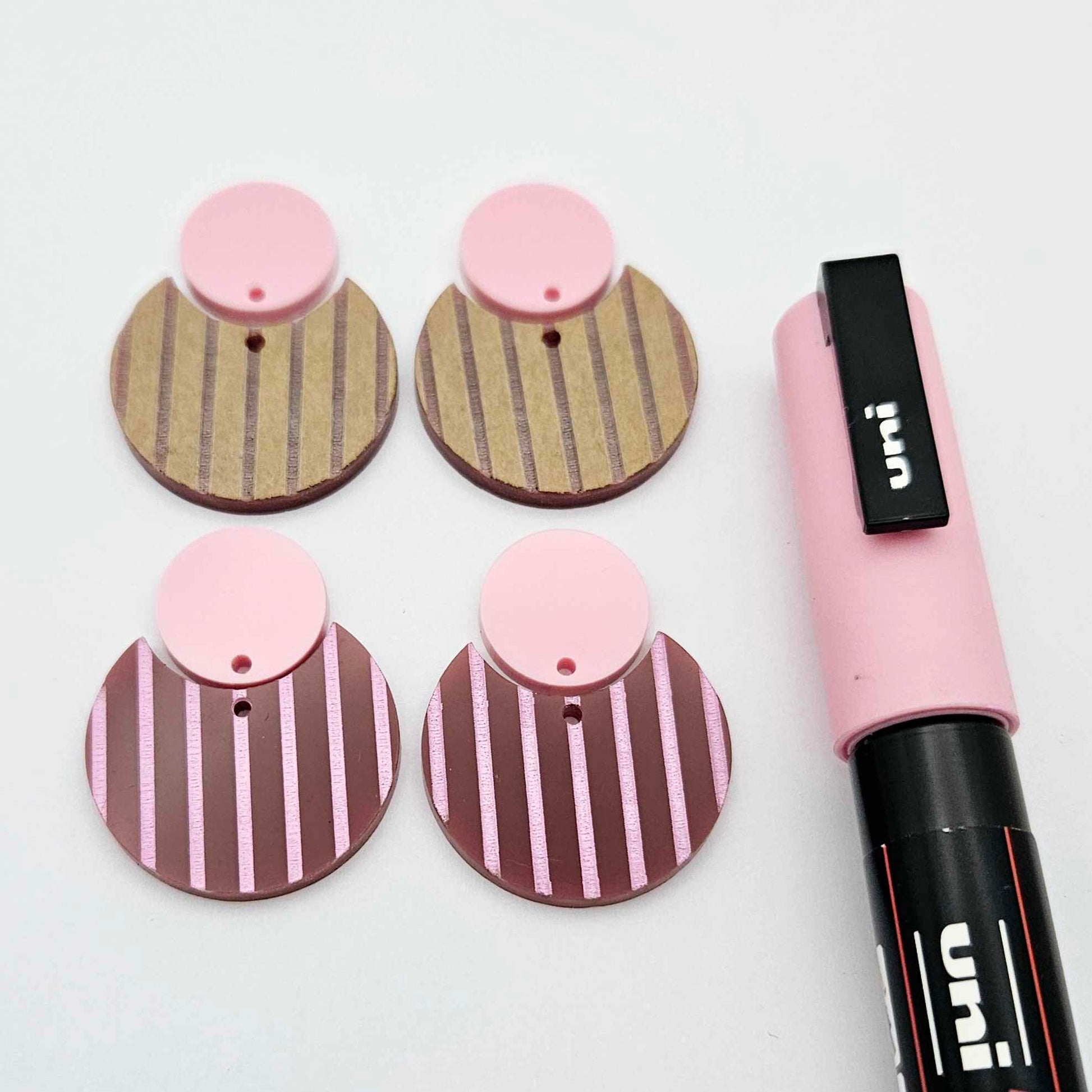 Nested circle dangle blanks showing one pair paint filled light pink and peeled, with another pair unpainted and with protective film on, pictured with a pink Posca paint pen