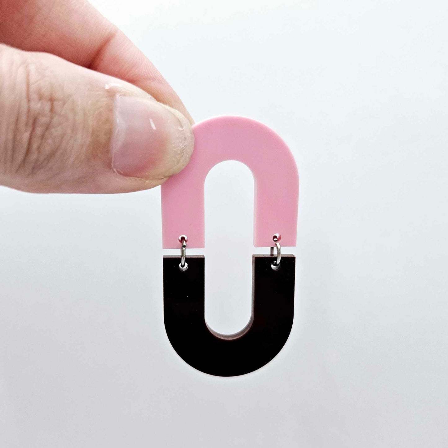 Layered U shape dangle earring in pastel pink and chocolate brown acrylic, assembled into an open oval design hanging as a statement stud dangle