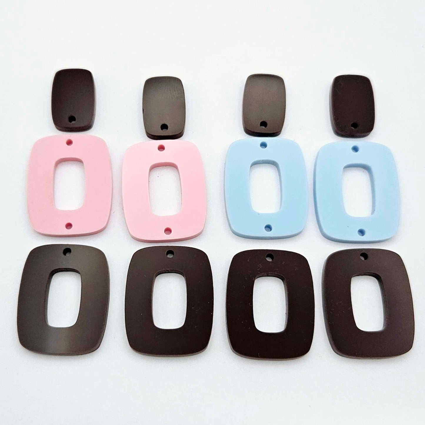 Two pairs of layered rectangle dangle blanks in chocolate brown and pastel pink/blue acrylic, unassembled pieces laid flat showing three-piece design