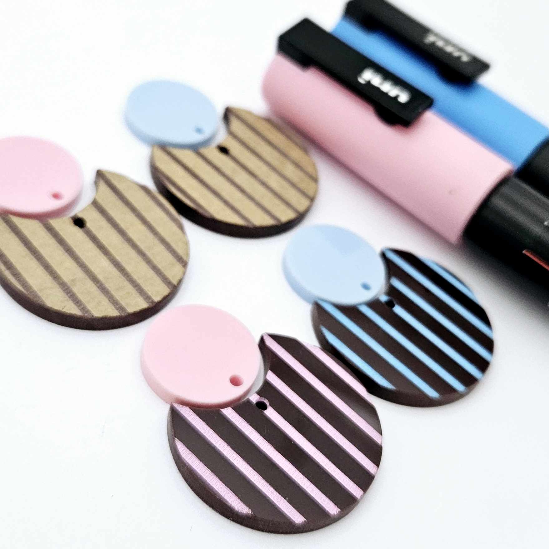 Nested circle dangle blanks showing one piece paint filled light pink and one piece paint filled light blue and peeled, with another pair unpainted and with protective film on, pictured with pink and blue Posca paint pen